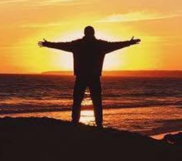 Man looking out to see on a rock with sunset